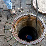 Worker inspecting a manhole cover on paved ground at Blue Box Self Storage.