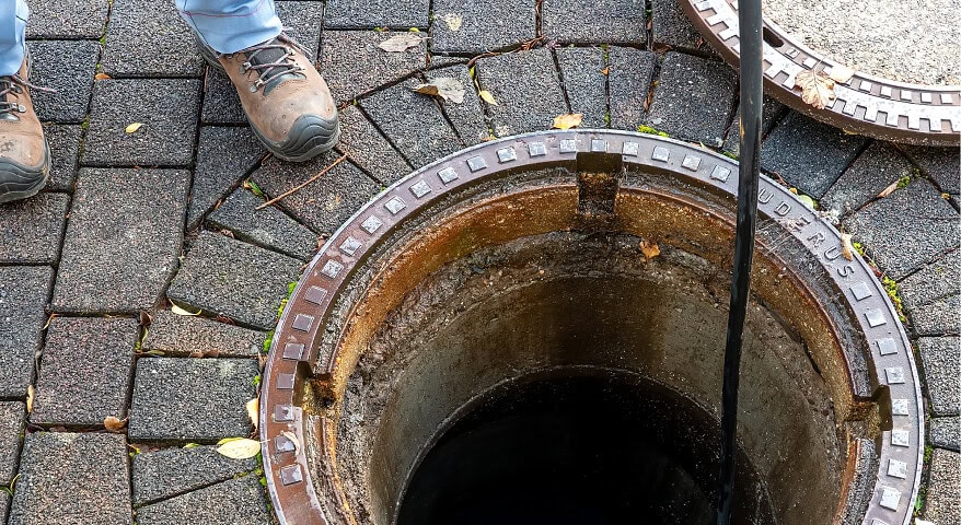 Worker inspecting a manhole cover on paved ground at Blue Box Self Storage.