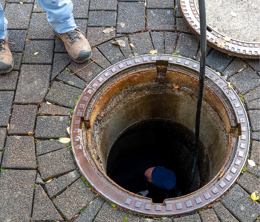 Worker inspecting a manhole cover on paved ground at Blue Box Self Storage.