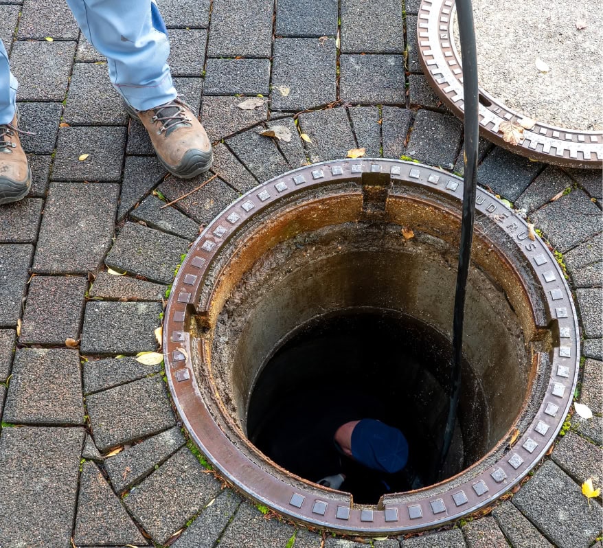 Worker inspecting a manhole cover on paved ground at Blue Box Self Storage.