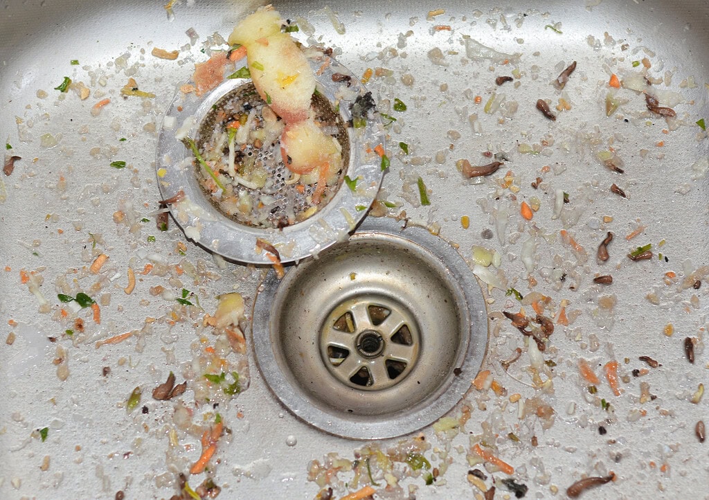 Kitchen sink drain clogged with food waste and grime buildup.
