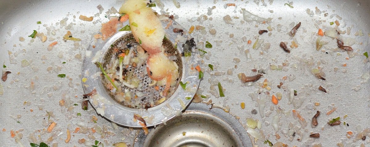 Kitchen sink drain clogged with food waste and grime buildup.