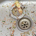 Kitchen sink drain clogged with food waste and grime buildup.