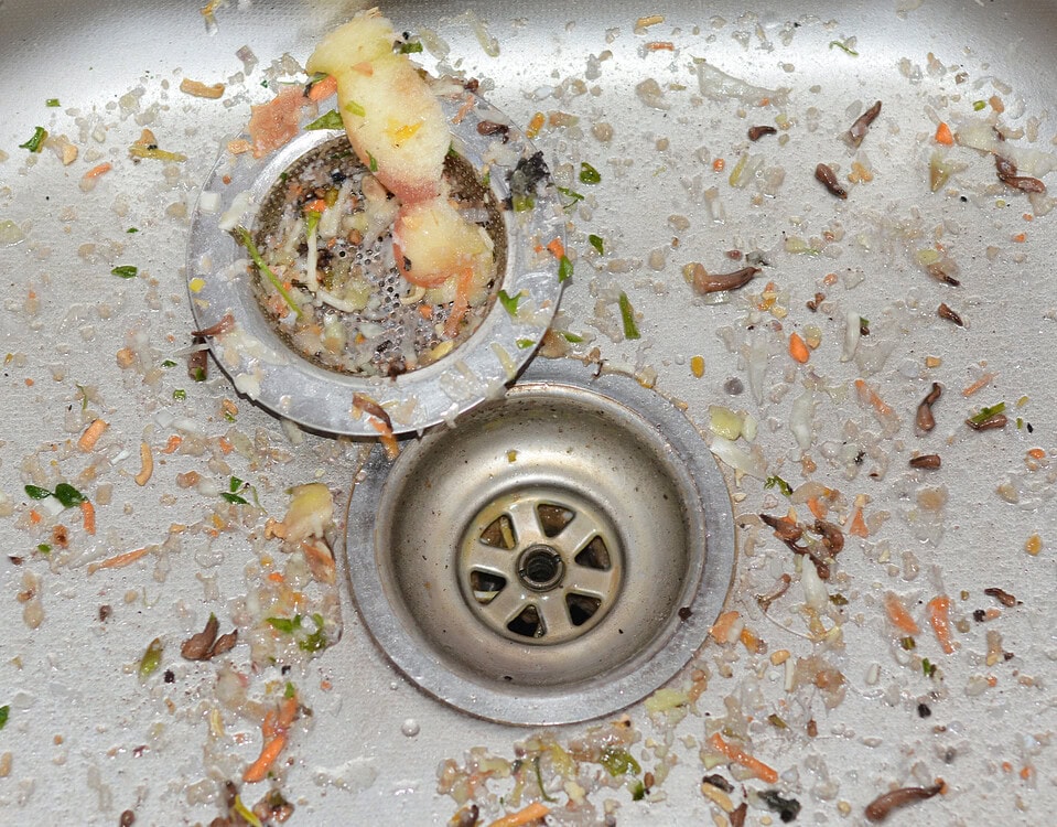 Kitchen sink drain clogged with food waste and grime buildup.