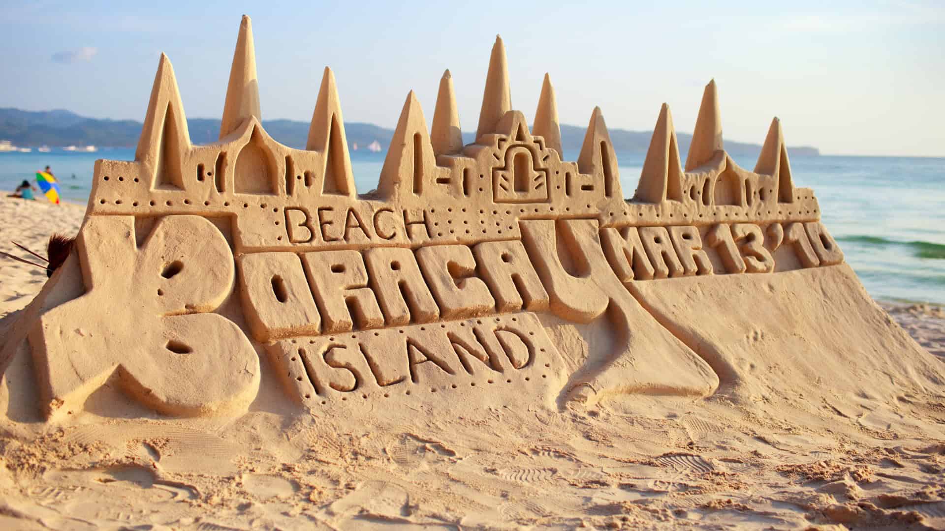 Intricate sand sculpture on a white sand beach with sea in background