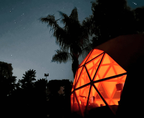 Unique geodesic dome glamping retreat under starry night sky with palm trees.