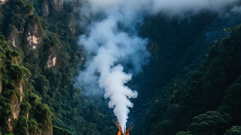 Peaceful mountain landscape featuring a traditional thatched hut emitting smoke amidst lush greenery.