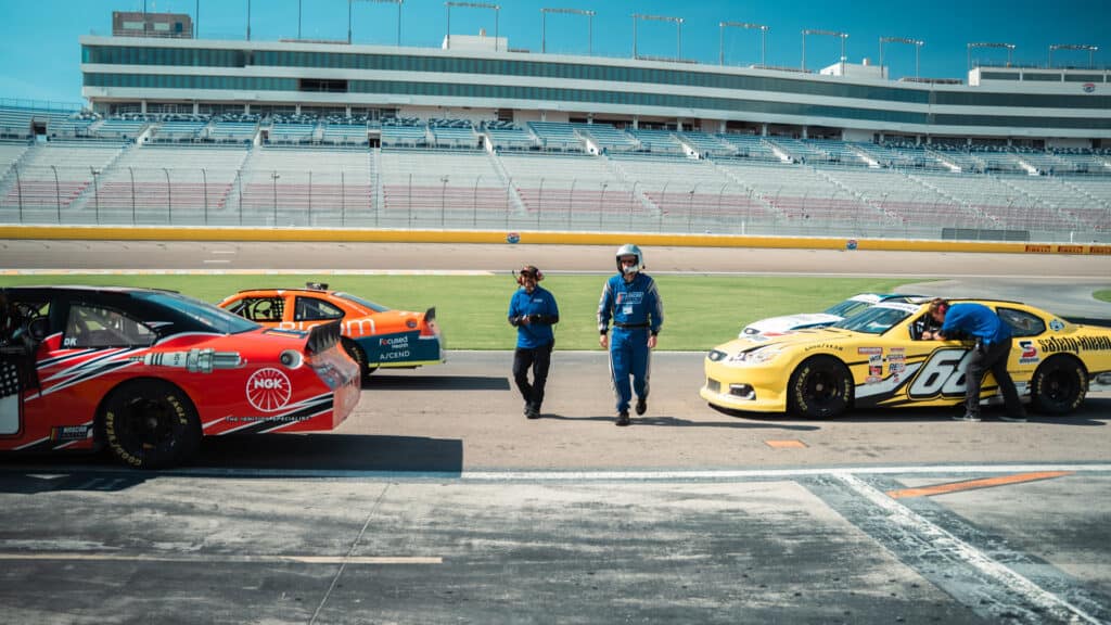 High-speed race cars in pit lane at a professional racing track during a motorsports event. Race car mechanics and team members preparing for the race at a busy, well-maintained racing circuit.
