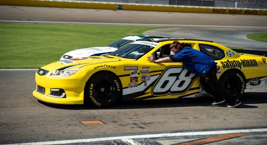 Fast race car pit stop with crew member pushing the yellow Chevrolet stock car, showing the excitement of motorsports and racing culture.