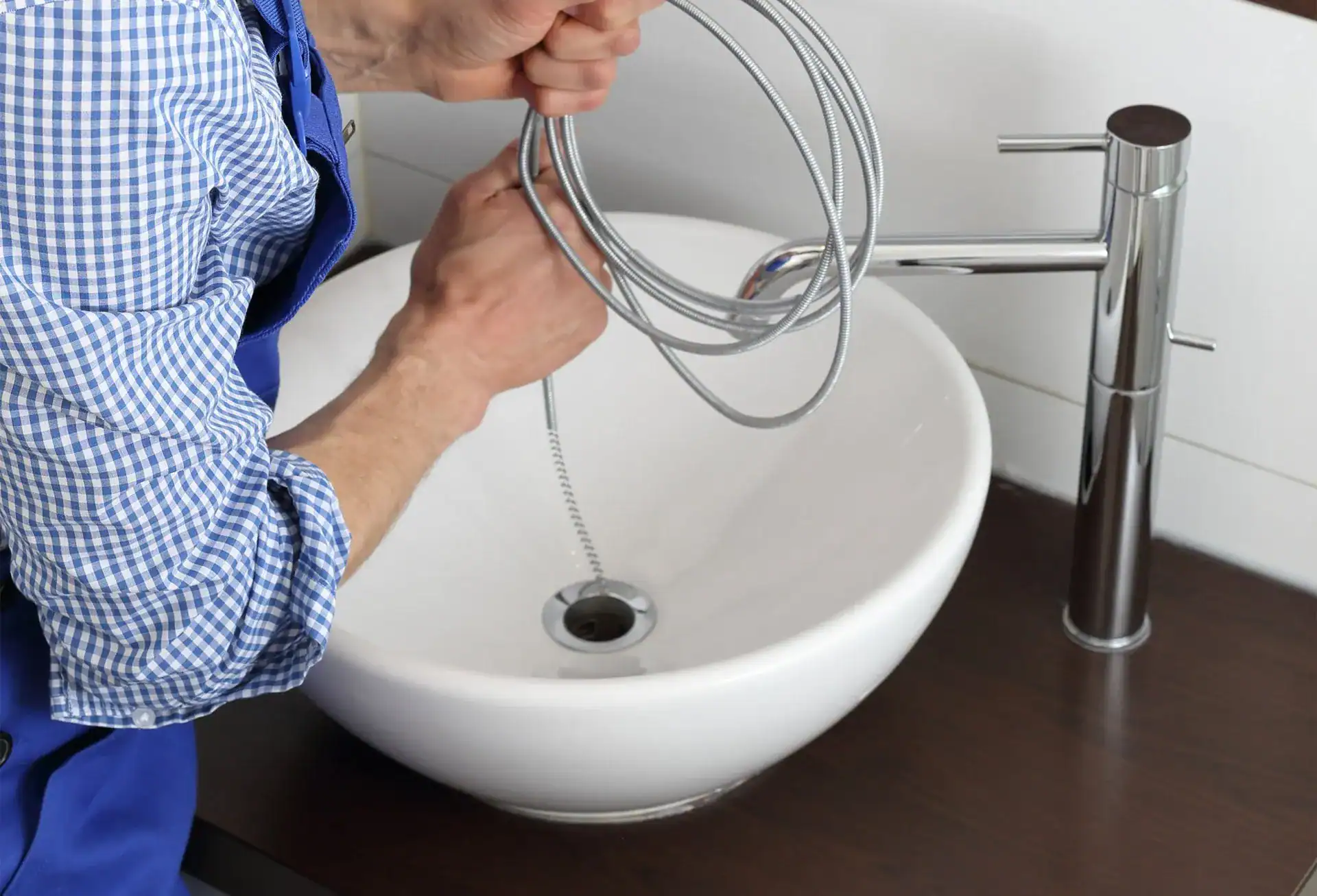 Plumber using a drain cleaning snake in a modern sink, showcasing advanced plumbing techniques for effective drain solutions.