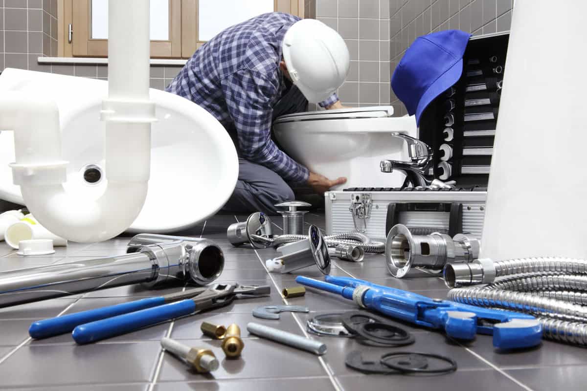 Plumber installing a toilet fixture in a bathroom, surrounded by plumbing tools and components, emphasizing expert faucet and fixture installation services.