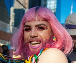 pessoa com barba e cabelos rosa em um desfile de parada do orgulho lgbtqia+