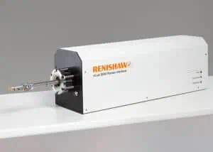 A Renishaw inLux SEM Raman interface device is displayed on a white surface against a neutral background. The instrument is a sleek, rectangular, white unit with black accents and features a protruding metallic arm equipped with a sample holder at the end. The device is branded with the Renishaw logo in orange and the model name "inLux SEM Raman interface" written below it. This advanced instrument exemplifies the integration of Raman spectroscopy with Scanning Electron Microscopy (SEM) for comprehensive material analysis, combining high-sensitivity molecular and chemical characterisation with detailed imaging.