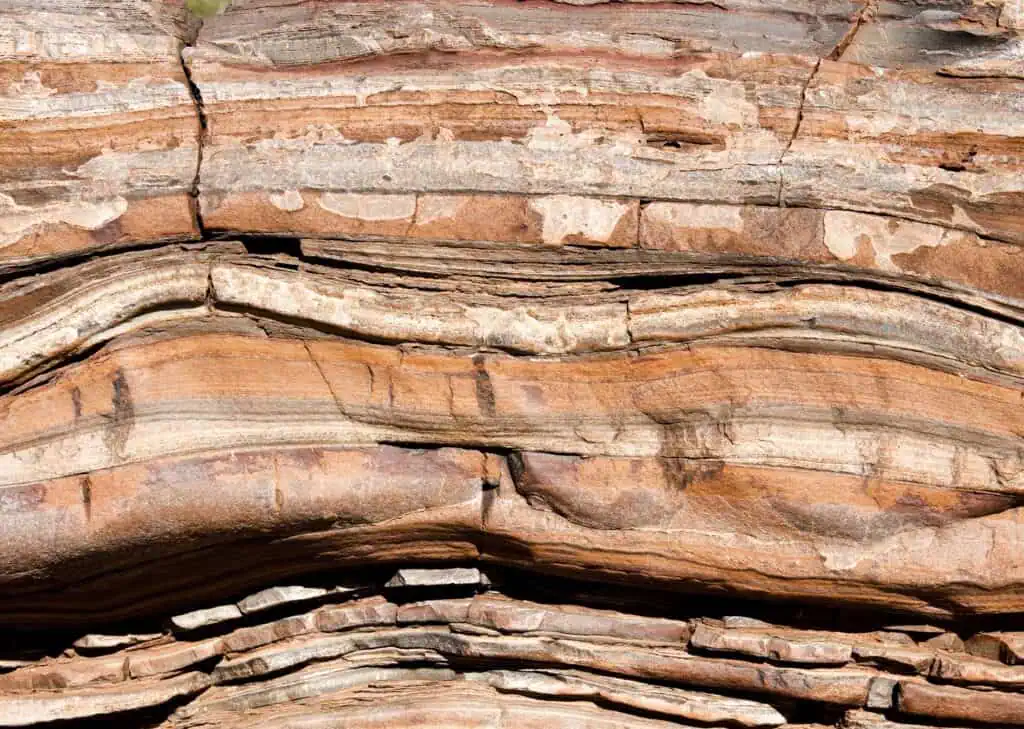 Close-up of layered geological rock formations with visible striations and folds, illustrating the natural structure and composition of rocks. Perfect for demonstrating geochemical and geological analysis techniques like XRF, XRD, and Raman spectroscopy used for mineral identification and elemental mapping. Image highlights the intricate details of rock samples for academic and industrial applications.
