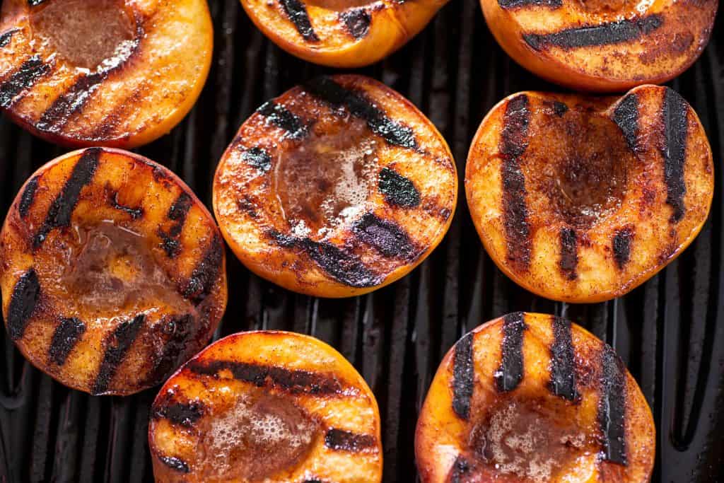 Juicy grilled peaches with charred grill marks on a barbecue grill.