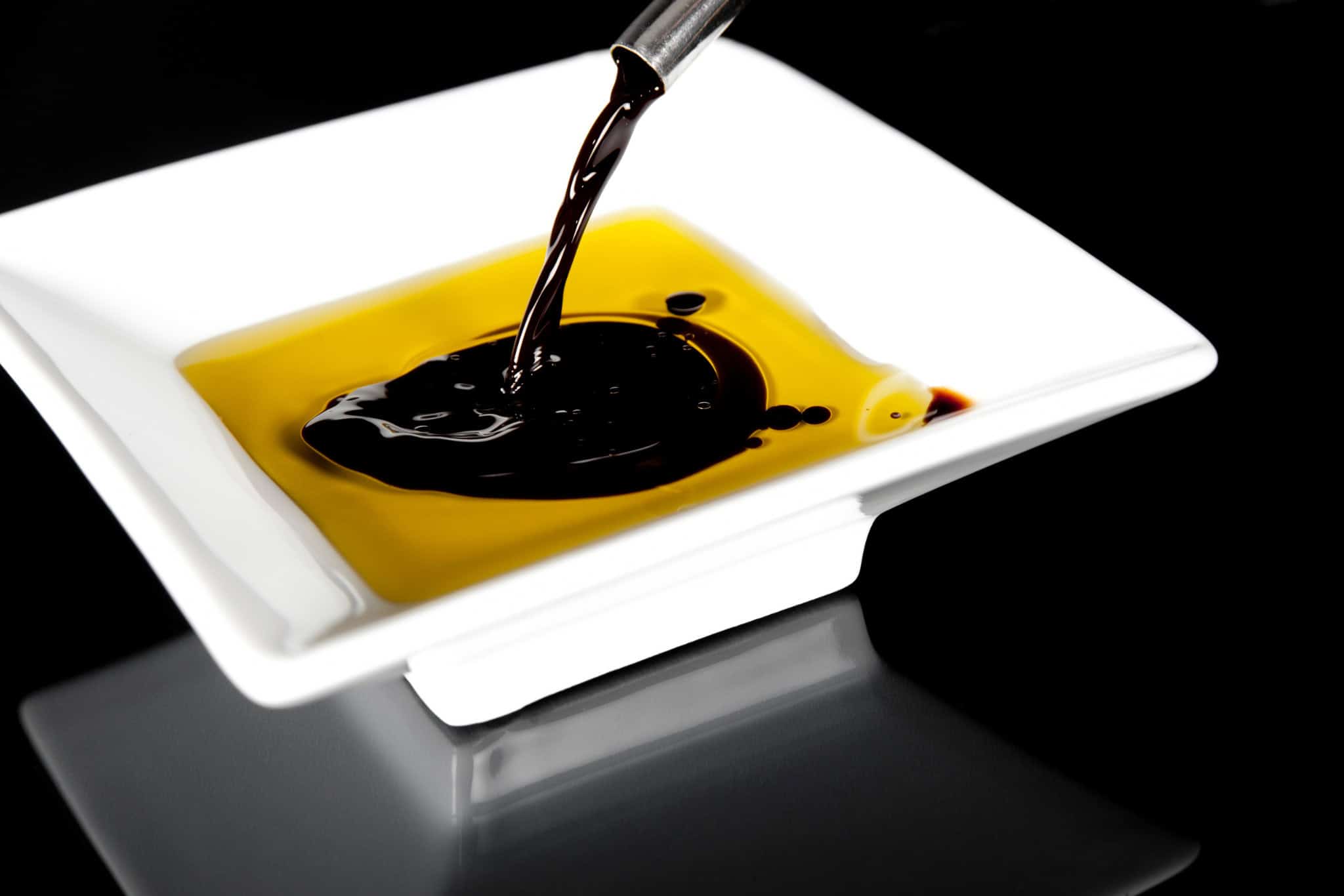 Rich balsamic vinegar and olive oil being poured onto a white plate, enhancing flavors in gourmet cooking. Perfect for salads, appetizers, or dipping bread in culinary dishes.