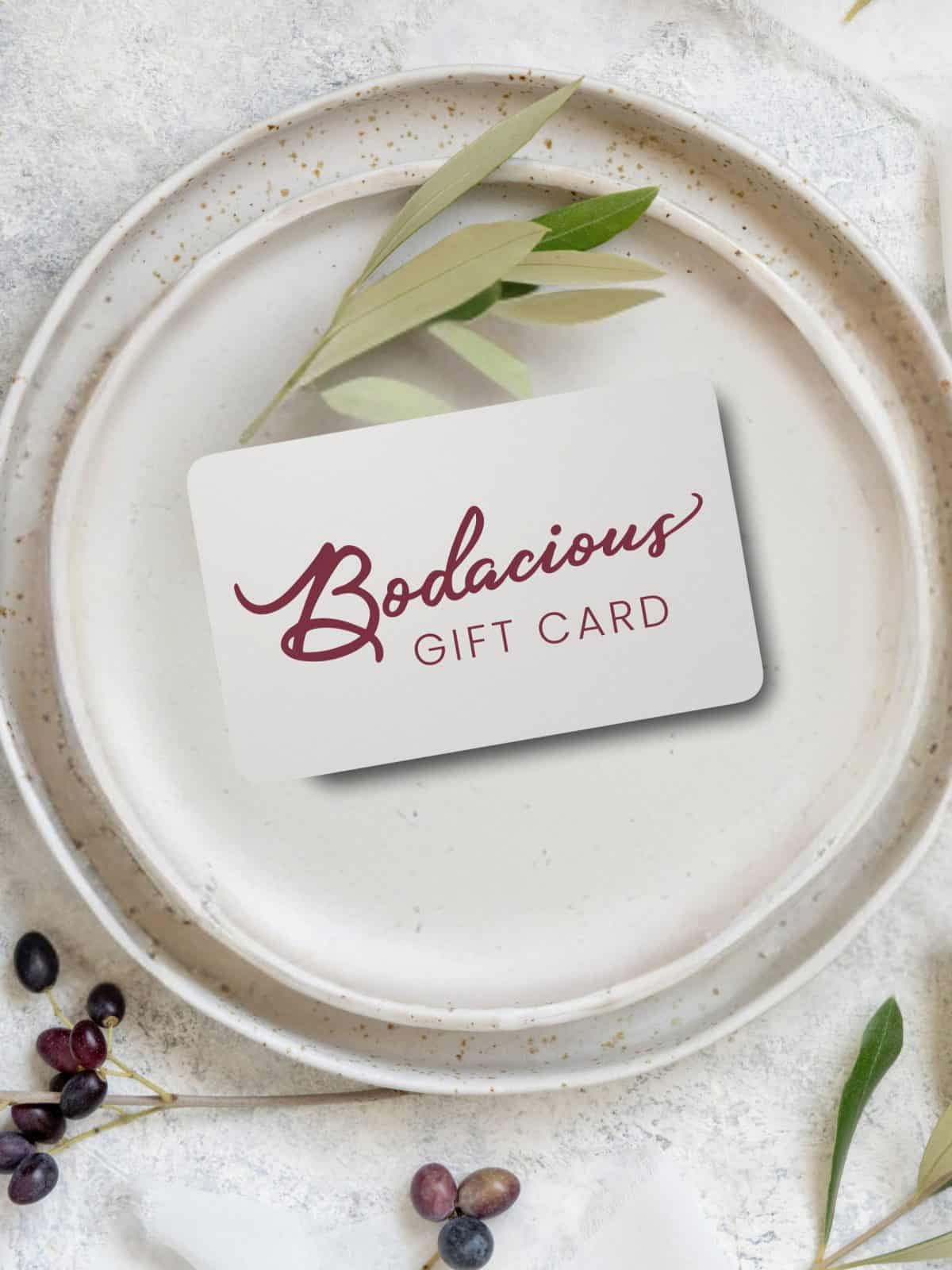 Elegant Bodacious Shops gift card on ceramic plate with greenery and berries, perfect for gift-giving, stylish floral design, and versatile for various occasions.