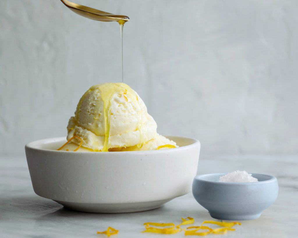 Butter drizzling over a scoop of vanilla ice cream in a white bowl with lemon zest; fresh, creamy, and dessert for summer, high-quality image for Bodacious Shops.