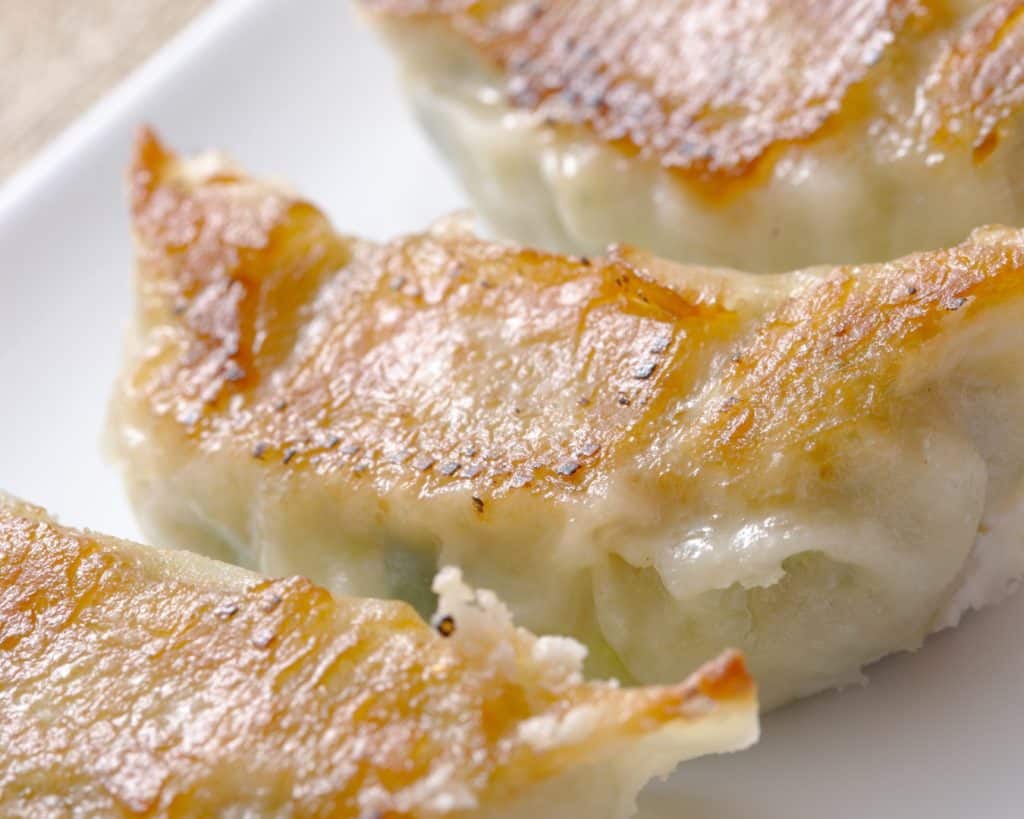 Crispy pan-fried dumplings with golden-brown crust and juicy filling, served on a white plate for a delicious Asian-inspired appetizer or snack.