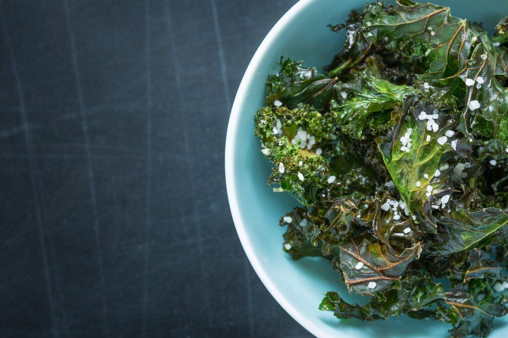 Fresh kale salad topped with coarse sea salt in a light blue bowl.