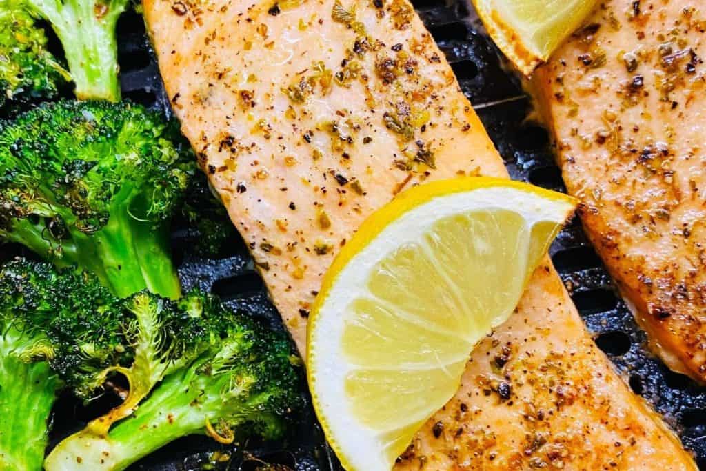 Succulent grilled salmon fillets seasoned with herbs served with fresh lemon wedges and grilled broccoli, perfect for healthy dining.