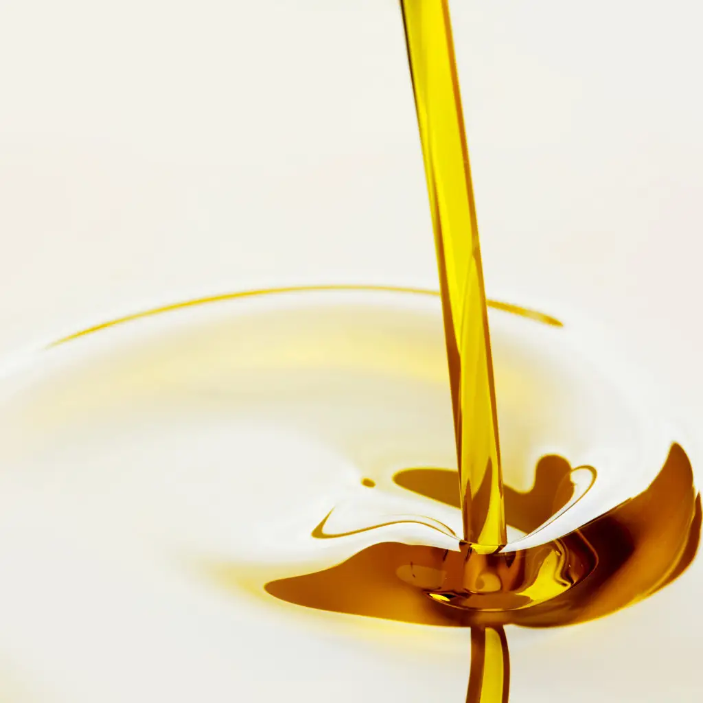 Golden liquid oil being poured, close-up of olive oil or cooking oil in a splash, high-quality food oil for cooking or salad dressing, vibrant stream creating ripples on a white surface, perfect for culinary or health-related topics.