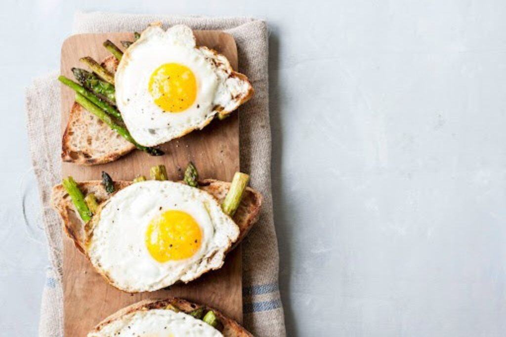 Sunny side up eggs on whole grain toast with asparagus on a wooden board, healthy breakfast, fresh eggs, nutritious meal, breakfast with vegetables, rustic wooden table, easy breakfast recipe, appetizing brunch dish.