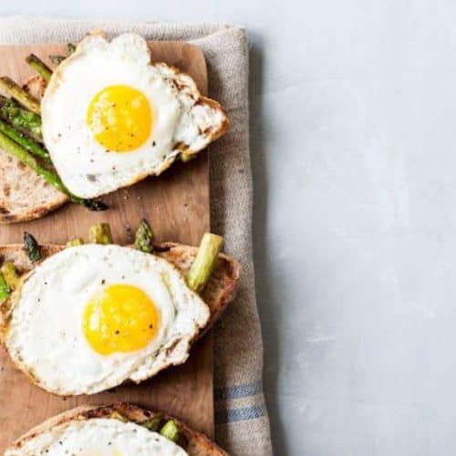 Sunny side up eggs on whole grain toast with asparagus on a wooden board, healthy breakfast, fresh eggs, nutritious meal, breakfast with vegetables, rustic wooden table, easy breakfast recipe, appetizing brunch dish.