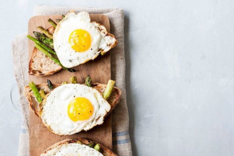 Sunny side up eggs on whole grain toast with asparagus on a wooden board, healthy breakfast, fresh eggs, nutritious meal, breakfast with vegetables, rustic wooden table, easy breakfast recipe, appetizing brunch dish.