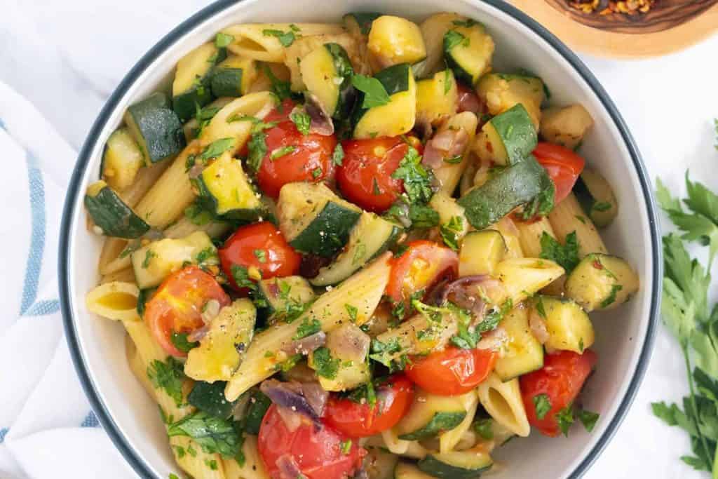 Fresh zucchini, cherry tomatoes, and pasta salad with herbs in a white bowl for healthy eating and summer recipes.