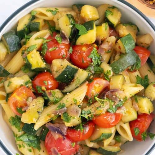 Fresh zucchini, cherry tomatoes, and pasta salad with herbs in a white bowl for healthy eating and summer recipes.