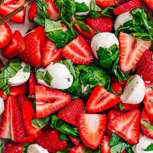 Fresh strawberry and basil salad with mozzarella cheese on a white platter, showcasing vibrant red strawberries, green basil leaves, and creamy mozzarella balls for a healthy and flavorful dish.