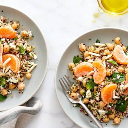 Fresh chickpea and quinoa salad with orange slices and mint on white plates, healthy vegetarian dish.