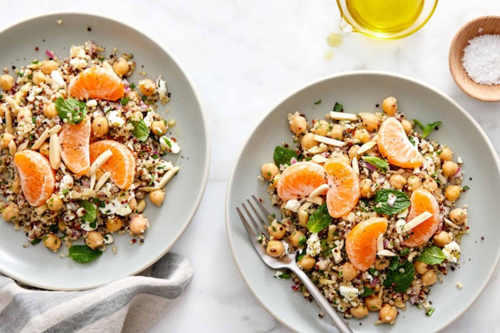 Fresh chickpea and quinoa salad with orange slices and mint on white plates, healthy vegetarian dish.