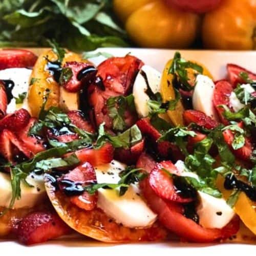 Fresh Caprese Salad with Strawberries, Basil, and Balsamic Glaze on a White Platter.