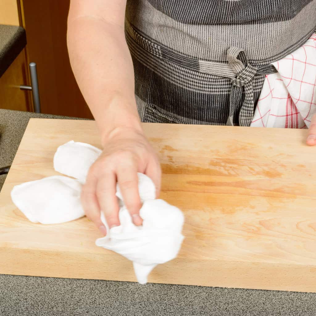 Soft white cleaning cloth being used to wipe a light wooden countertop in a kitchen setting. Kitchen cleaning and maintenance with cloth, close-up.