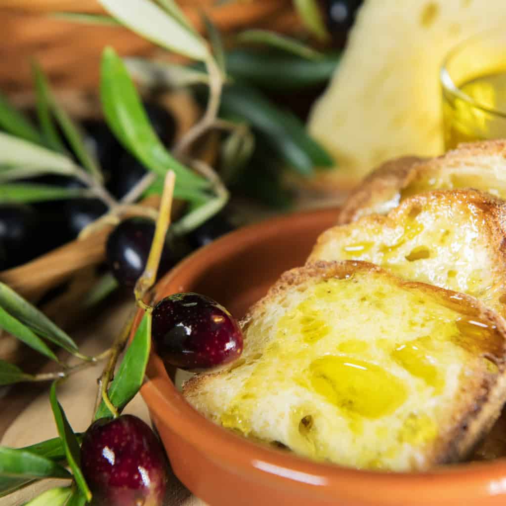 Olive plant with fresh black olives and Italian bread topped with melted cheese, garlic, and olive oil in a rustic setting.