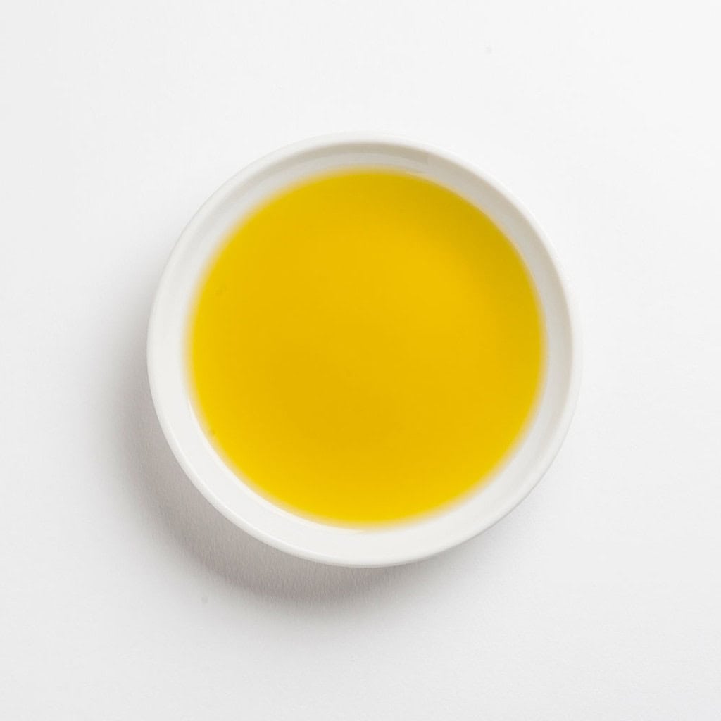 Bright yellow olive oil in a white ceramic bowl on a white background.