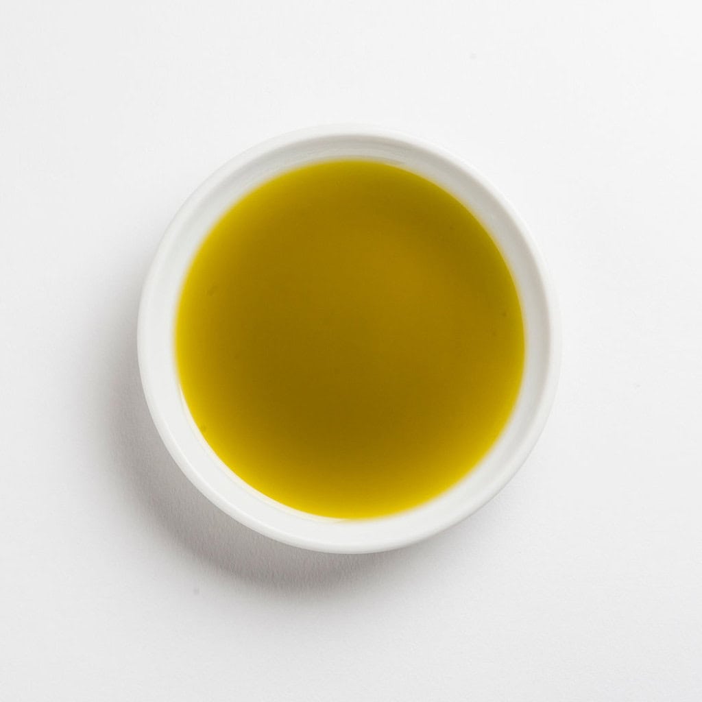 Smooth green olive oil in a white bowl, top view.