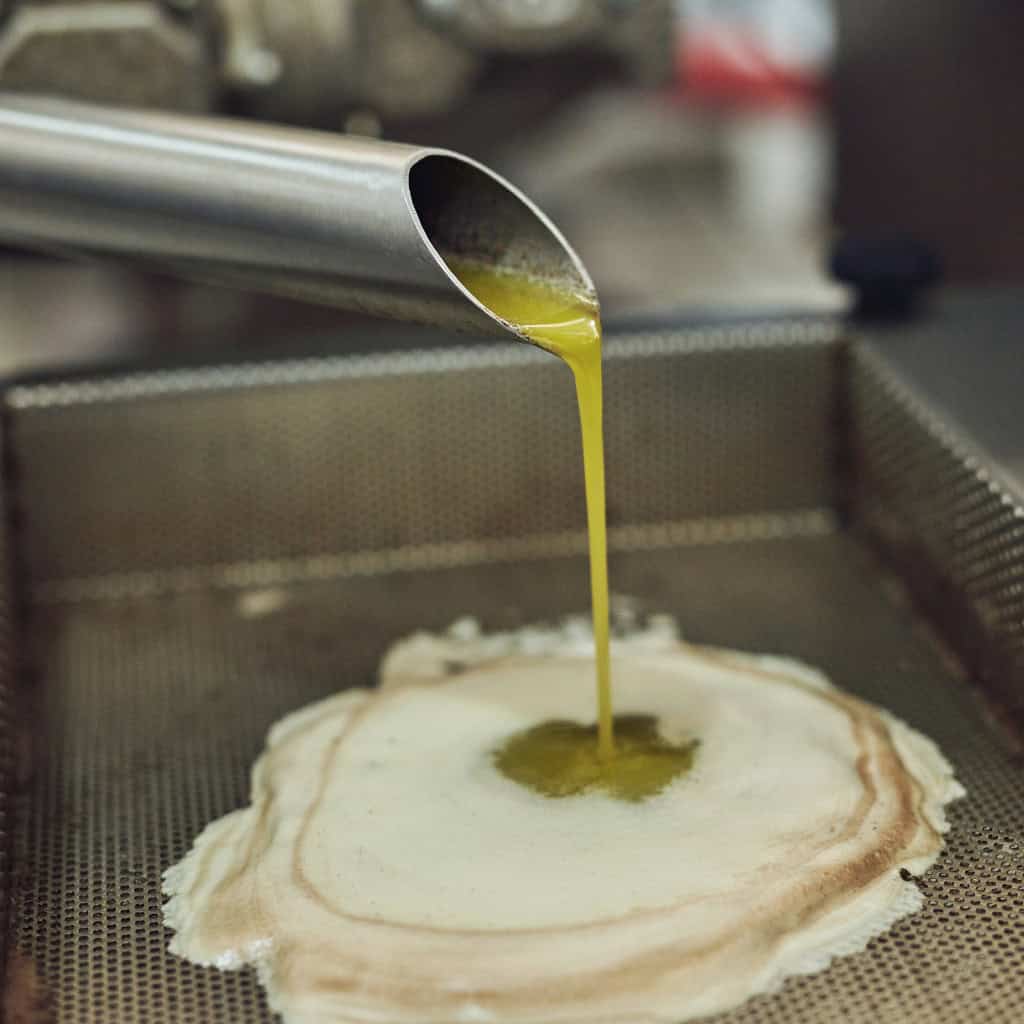 Golden olive oil being poured over a freshly cooked crepe on a griddle.