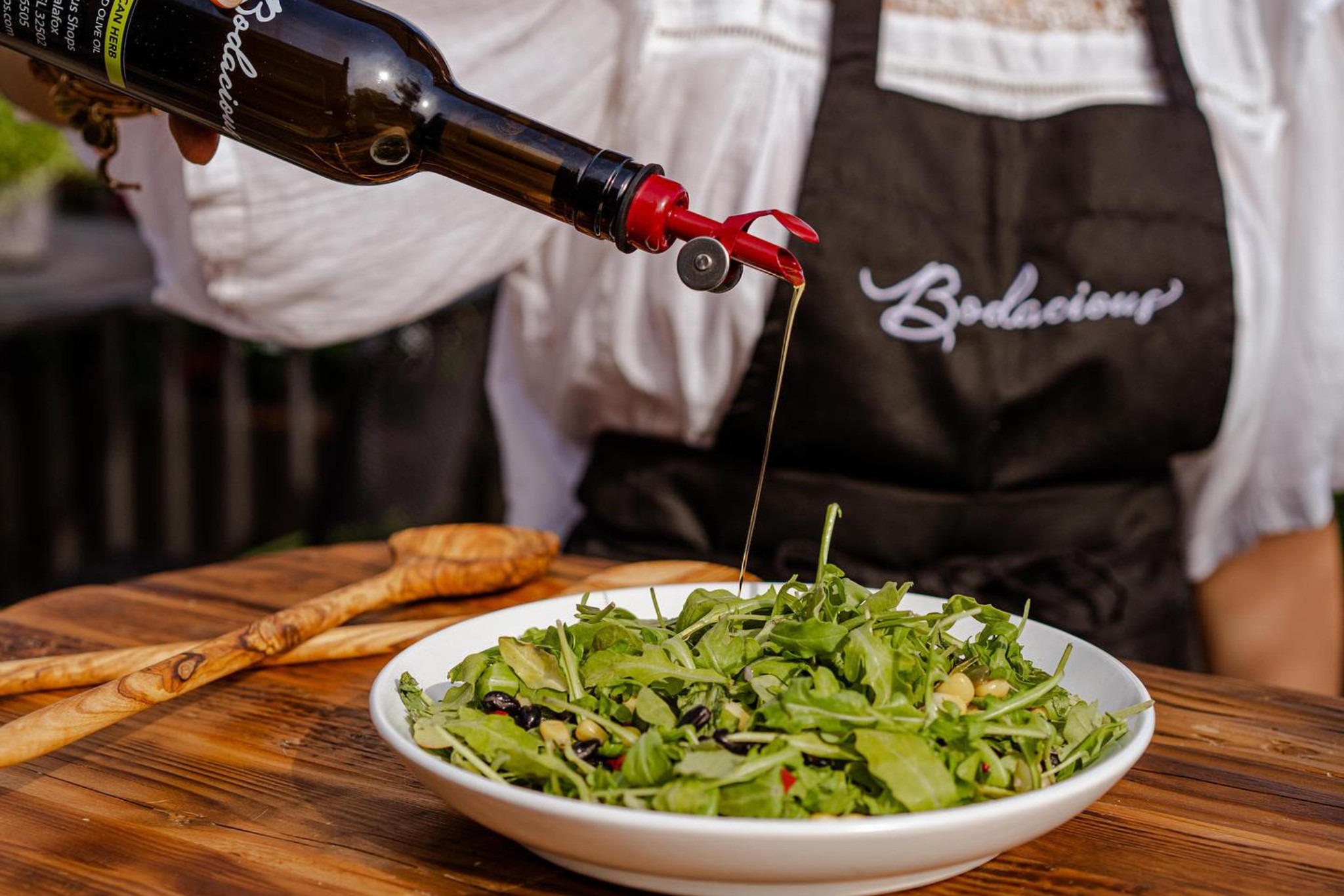 Fresh arugula salad drizzled with balsamic vinegar for a tasty, healthy meal. Served outdoors with a wooden spoon on a rustic table, highlighting quality food and culinary experiences from Bodacious Shops.