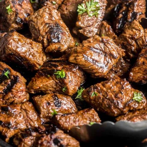 Succulent grilled beef chunks glazed with savory sauce, garnished with fresh herbs in a cast iron skillet. Perfect for barbecue dinners and meal prep.