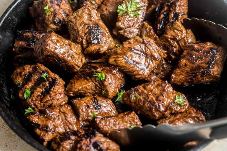 Succulent grilled beef chunks glazed with savory sauce, garnished with fresh herbs in a cast iron skillet. Perfect for barbecue dinners and meal prep.