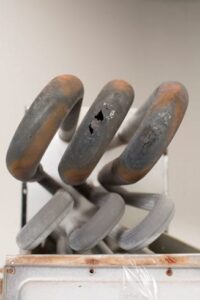 Close-up of a rusted and corroded heat exchanger with visible holes and cracks, likely from a water heater.
