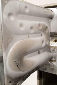 A metal sheet with circular indentations, possibly from heat exchangers, is cracked near its lower section. The surface appears slightly worn and is part of a larger structure.