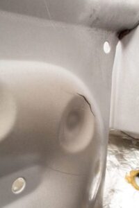 Close-up of a cracked metal surface on a heat exchanger, revealing a visible fracture line and smooth surrounding area, with a few rounded indentations and small fasteners in view.