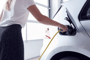 In a Bonfe Insider feature, a person in a white shirt and black skirt plugs a yellow charging cable into a sleek white electric car inside the garage—a snapshot of innovation from March 2022.