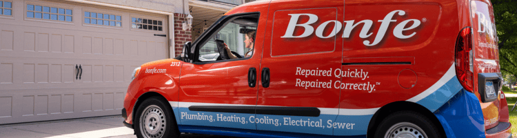 A red Bonfe service van offering plumbing, heating, cooling, electrical, and sewer emergency services is parked in front of a house garage.
