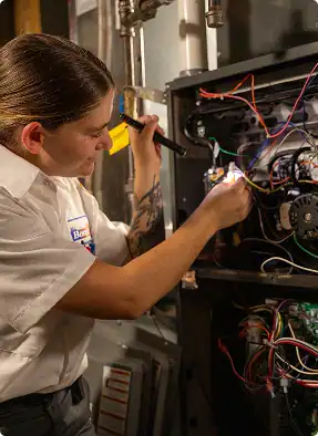 A technician examines and repairs the wiring inside an open heating or furnace unit using a flashlight, while customers can take advantage of special Financing Offers.