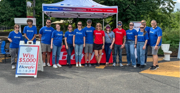 A group of people wearing blue and red Bonfe shirts stand in front of a Bonfe tent and a sign advertising a $5,000 giveaway, highlighting Bonfe’s commitment to community involvement.